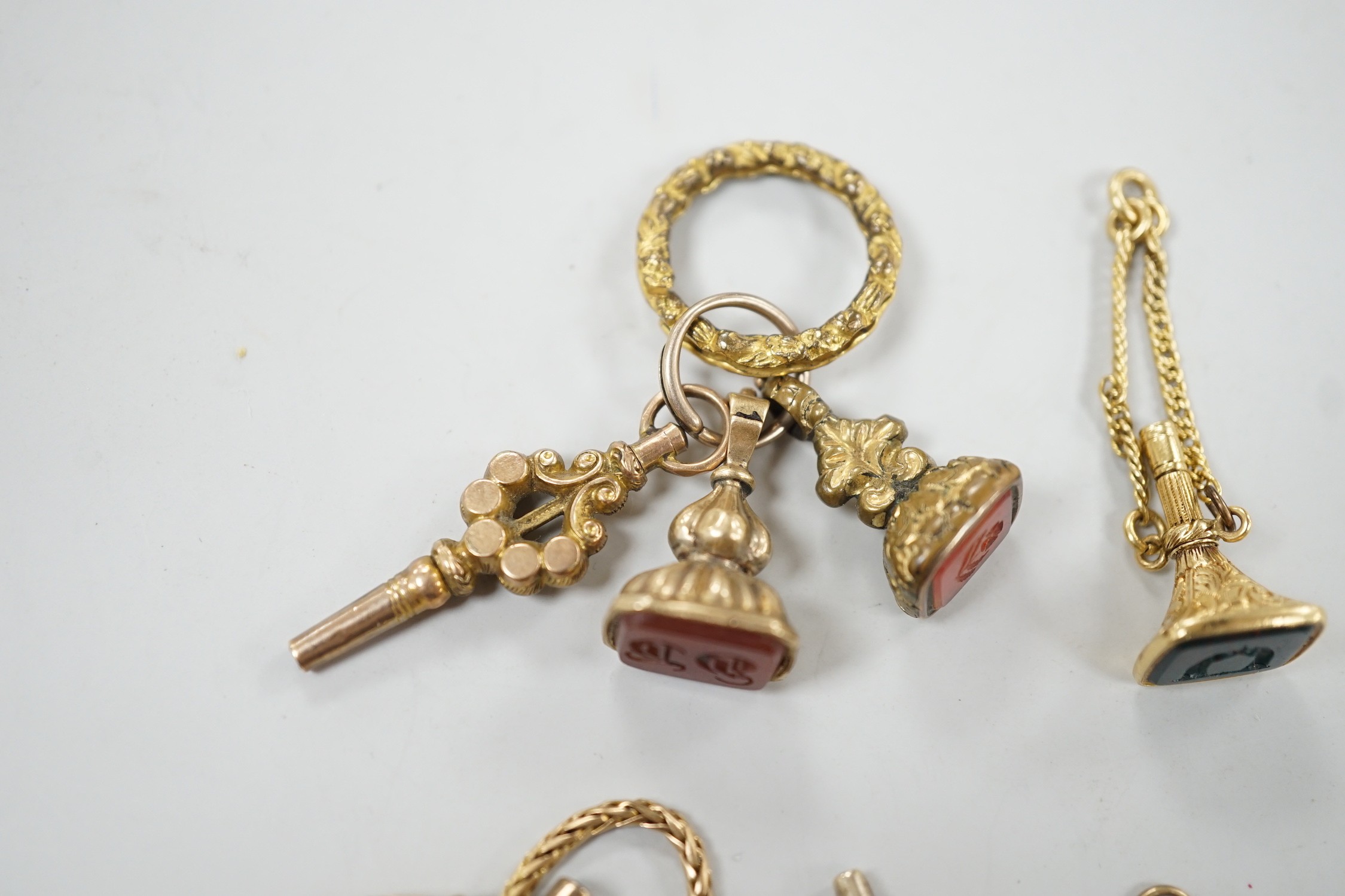 Two 19th century yellow metal overlaid and bloodstone set watch key fobs, one of funnel form, 21mm, a similar gold plated and carnelian set watch key fob, two other fob seals and a watch key on chain.